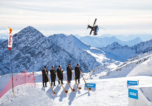 Alphornbläser auf Skipiste Freeskier springt in der Luft beim Freeski Finale 2022