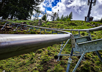 Blick entlang einer Schiene einer Sommerrodelbahn auf einer grasbewachsenen Anhöhe