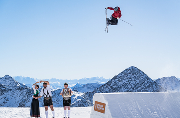 Freeskierin Lara Wolf spring über ersten Kicker beim Training für den FIS Freeski World Cup Stubai und Schuhplattler stehen daneben am Knuckle